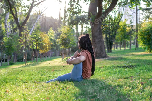 Preview: Beautiful young woman with long African braids is doing yoga outside in a park.
