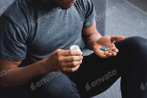Preview: cropped view of african american man taking pills at home