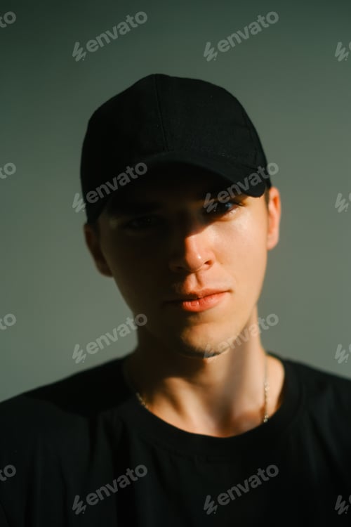 Preview: Portrait of stylish handsome caucasian man fashion model in t shirt and cap, studio shot.