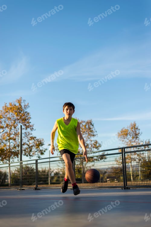 Preview: Young boy dribbling a basketball on an outdoor court.