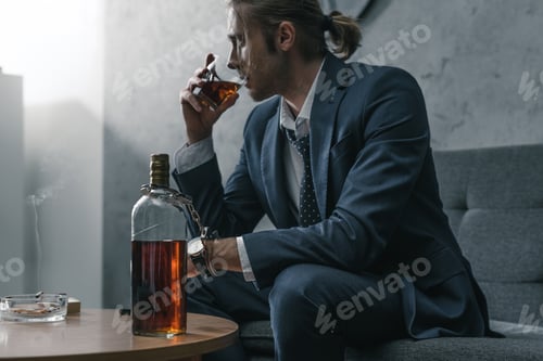 Preview: alcohol addicted businessman with glass and bottle of whiskey sitting on couch