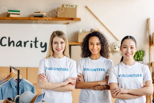 Preview: three beautiful multicultural volunteer girls with crossed arms smiling and looking at camera