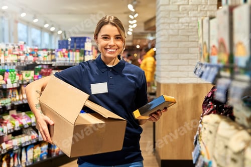 Preview: Smiling supermarket worker stocking shelves with products