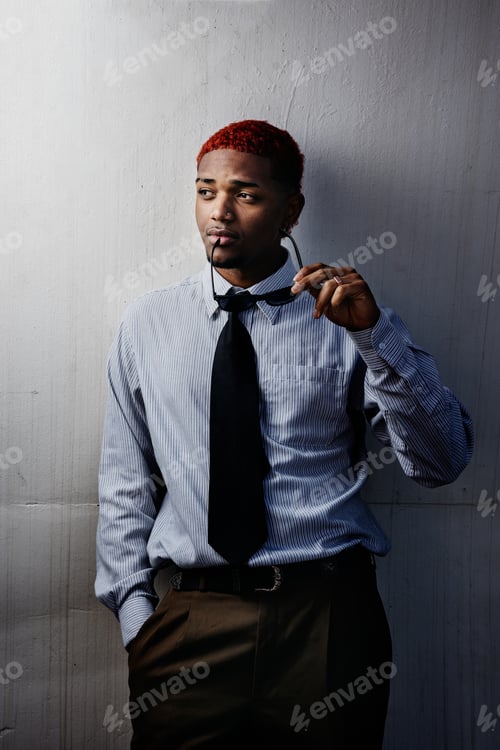 Preview: Portrait of an executive man leaning against a wall looking away with sunglasses in his hand