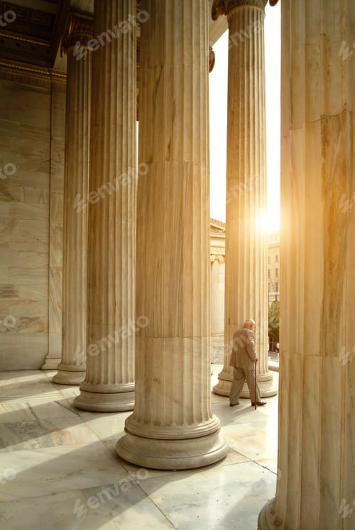 Preview: Elderly individual walking between towering columns at sunset.