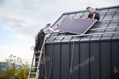 Preview: Technicians carrying photovoltaic solar module while installing solar panel system on roof of house