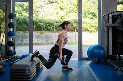 Preview: Woman doing dumbbell lunge exercise in gym