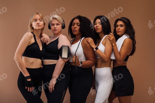 Preview: Five diverse females in sports clothes with fitness accessories standing together in studio