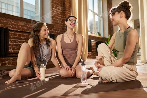Preview: Young Adult Caucasian Women Sitting on Yoga Mats Smiling and Conversing