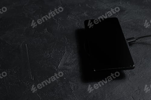 Preview: wireless charging pad for mobile phone. Black background. Top view. Space for text