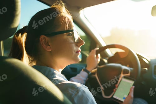 Preview: Happy woman uses a navigator in a smartphone while driving a car