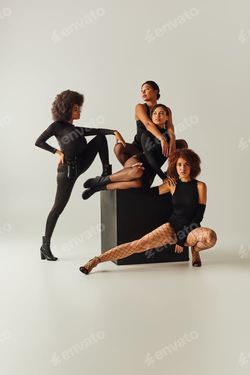 Preview: appealing african american women in sexy bodysuits posing together on black cube, fashion concept