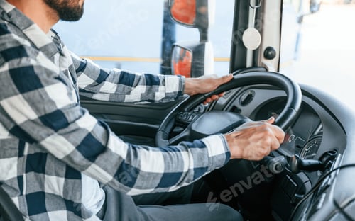 Preview: Sitting in the cabin by steering wheel. Young truck driver is with his vehicle at daytime