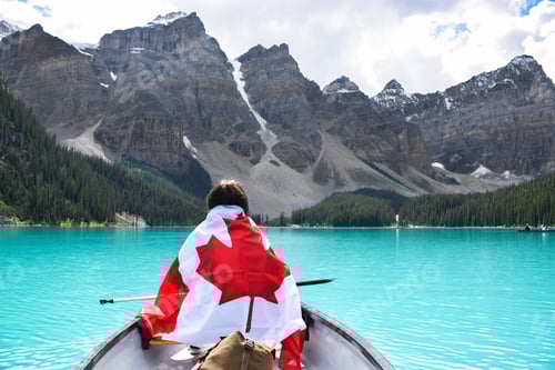 Preview: Young girl wrapped in a Canadian flag riding in a canoe on turquoise lake surrounded by mountains