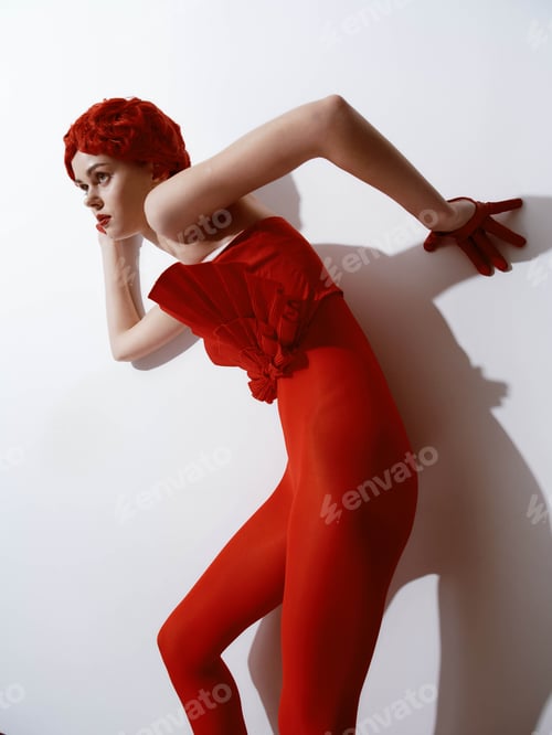 Preview: Confident woman in red dress posing against wall with hands on hips in stylish fashion portrait