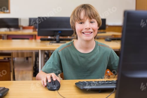 Preview: Male child student smiling while using desktop computer and wired mouse at school computer lab desk