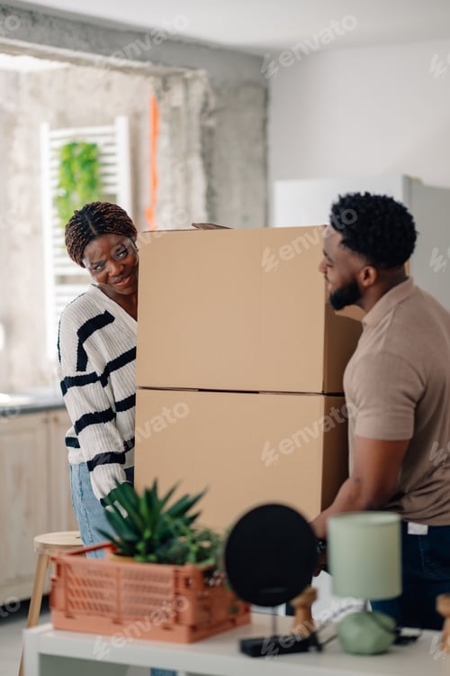 Preview: Happy couple carrying stacked cardboard boxes into new home