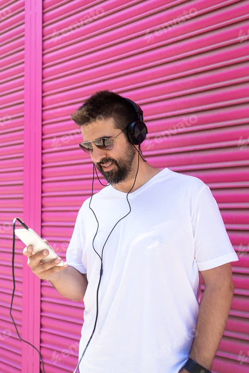 Visualização: Homem barbudo com fones de ouvido e óculos de sol usando um smartphone enquanto ouve música