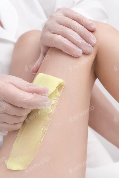 Preview: Closeup view of cosmetologist removing hair on female leg using hot wax in professional beauty salon