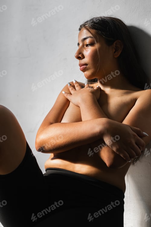 Preview: covering her breasts with her hands folded while leaning against the wall with a sad look