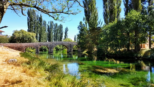 Preview: Idyllic landscape with stone bridge over transparent green river.