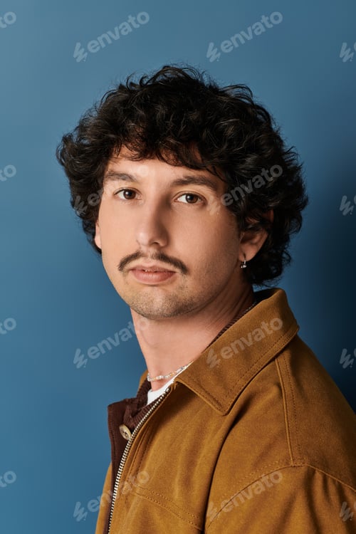 Preview: Stylish young man poses confidently against a vibrant blue backdrop showcasing modern fashion trends