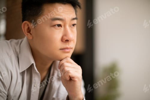 Preview: Closeup of unhappy asian middle aged man sitting alone at home, leaning on his arm, have heavy