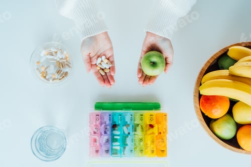 Preview: Female hands with green apple and different pills. Choose between natural and traditional