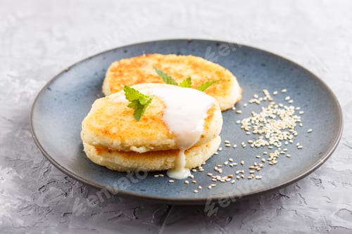 Preview: Cheese pancakes on a blue ceramic plate with milk sauce on a gray concrete background.