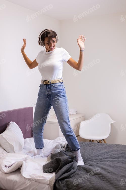 Preview: Happy woman in casual clother at home in bedroom listen music in headphones dancing jumping smiling