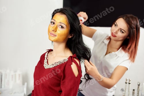Vista previa: La mujer usa darsonval para masajear la piel del cabezal, con máscara dorada en la cara en un salón de belleza.