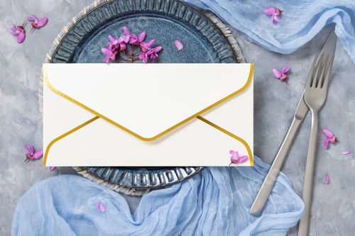 Preview: Wedding table place with envelope near fabric and wild purple flowers top view on gray, mockup