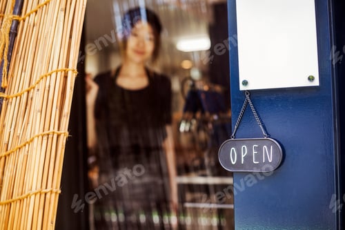 Preview: Open sign on glass door to a bakery, a woman standing in the doorway.