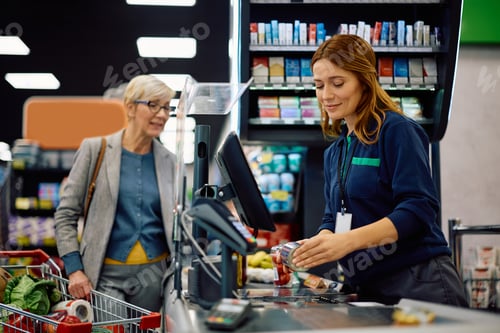 Preview: Smiling supermarket cashier scanning customer's groceries at checkout