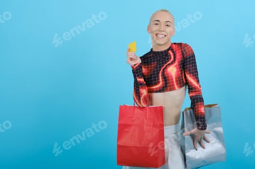 Preview: Young happy non-binary model holding shopping bags and a credit card on an isolated background.