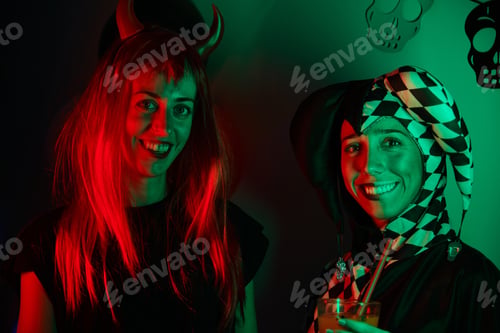 Preview: Two women dressed as a harlequin and devil smiling at a Halloween party.