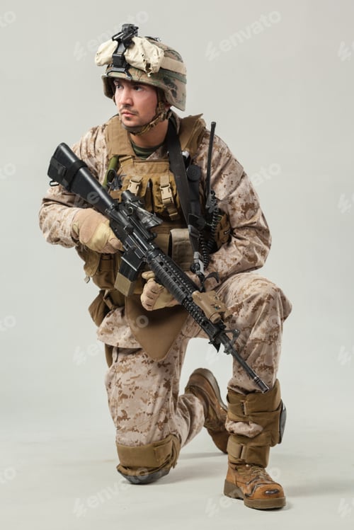 Preview: Soldier in military gear holds rifle while kneeling on light gray background