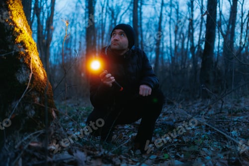 Preview: standing in the forest at night, a man uses a flashlight to search.