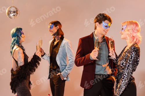 Preview: elegant nonbinary people in party masks holding champagne glasses and talking on beige background