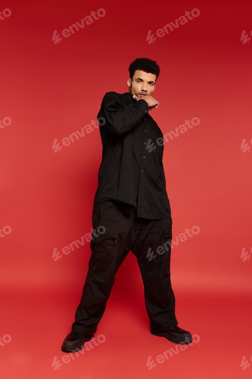 Preview: Young handsome man posing confidently against a vibrant red backdrop in casual attire