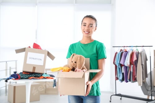 Preview: Young woman holding box with donations indoors