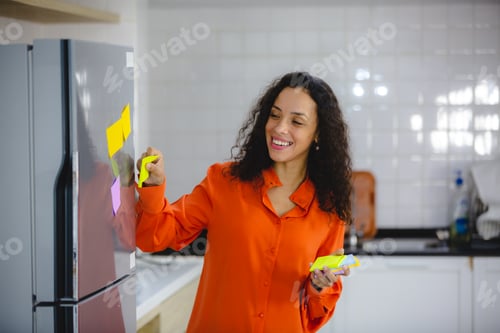 Preview: Young and organized female with curly hair in casual clothing making to-do and checklist
