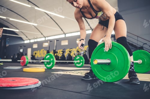Preview: Atheltic muscular woman cross fit training changing weight on barbell