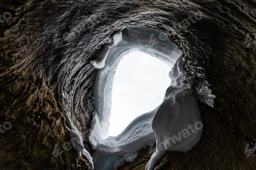 Preview: Shot through a textured eroded tunnel covered in snow with the light shining through the top