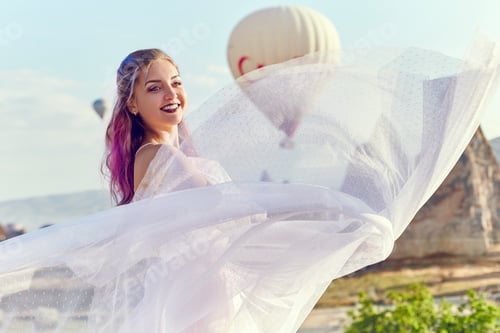 Preview: Woman in a long dress on background of balloons in Cappadocia. Girl with flowers hands
