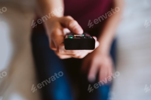 Preview: close up of unrecognizable woman holding remote tv control at home. Television and tech