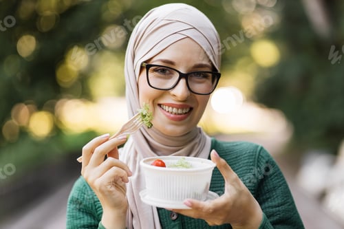 Preview: Close-up portrait of muslim business woman holding a vegetable salad in a plastic bowl