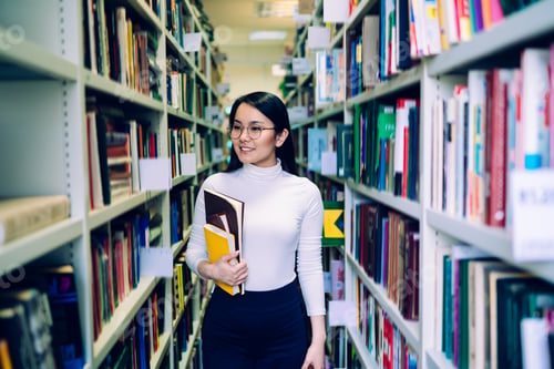 Preview: Cheerful Asian woman choosing book in library