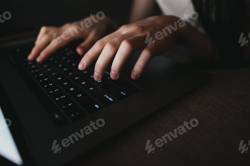 Preview: Woman is typing on a laptop keyboard while lying on a sofa at home in the dark