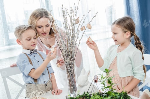 Preview: Happy mother with two children decorating willow branches with easter decorations